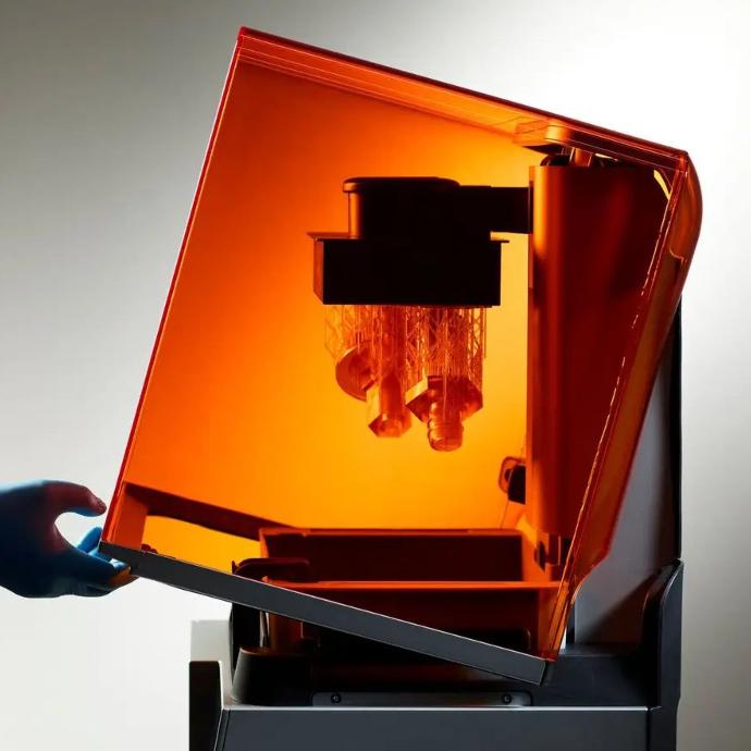 3D printer with orange cover open, showing printed parts on the build platform.